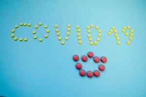 volumetric inscription of multi-colored pills on a blue paper background coronavirus. The crown is made of pink convex tablets for inscription. medicines for the treatment of viral infections photo