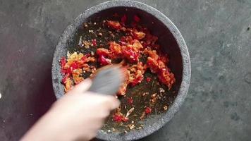 The process of making a chili sauce. A hand is pulverizing onions and chilies in a pestle on a stone mortar to make a chili sauce. video