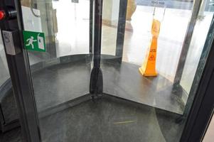 A revolving glass door to the shopping center, a building, a three-door structure anchored on the central shaft and rotating on a vertical axis and an orange sign to the wet floor photo