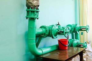 Leaking faulty valve, fitting on the pipeline with a bucket under it in the factory plant. Concept repair of pipe and valve with available tools photo