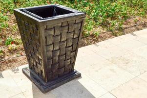 black wooden wicker trash for discarding garbage to maintain cleanliness is on the stone floor against the backdrop of the flowerbed photo