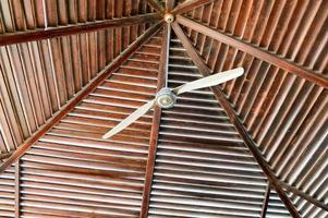 la textura de un techo de madera marrón es un resumen de las vigas de troncos dispuestas verticalmente horizontalmente y un gran ventilador de techo del calor. el fondo foto