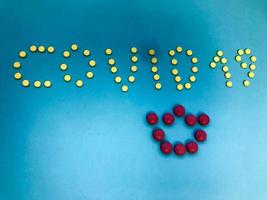 three-dimensional inscription of the letter from the tablets of bright color. word coronavirus with yellow round tablets. a bright pink volumetric crown is laid out from the drugs. drugs on photo