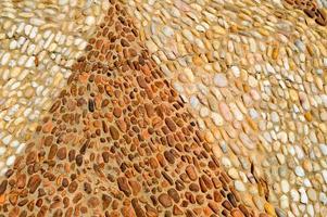 The texture of the stone wall, the road from small round and oval stones with abstract triangular patterns patterned triangle pyramid seams of natural old yellow black brown. The background photo