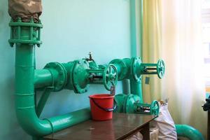 Leaking faulty valve, fitting on the pipeline with a bucket under it in the factory plant. Concept repair of pipe and valve with available tools photo