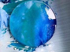 The process of creating a home-made trendy abstract modern pattern painted with a brush of acrylic blue multi-colored resin on a round wooden boar photo