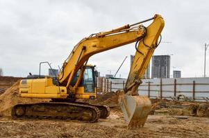 tractor de excavadora pesada industrial de gran alcance amarillo brillante, bulldozer, equipo de construcción especializado para la reparación de carreteras durante la construcción de un nuevo microdistrito en una gran ciudad foto