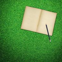 Pencil and old book open on green grass background photo