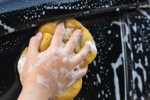alguien atrapa a mano una esponja amarilla lavando el auto con una pequeña burbuja. foto