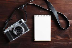 Blank notepad page and modern camera in classic style on dark brown wooden table photo