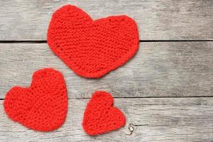 Three red knitted hearts on a gray wooden background, symbolizing love and family photo