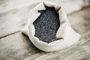 Poppy seeds in a burlap bag on a vintage wooden gray background. The tasty and useful seeds rich with protein and oils. photo