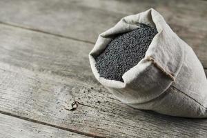 Poppy seeds in a burlap bag on a vintage wooden gray background. The tasty and useful seeds rich with protein and oils. photo