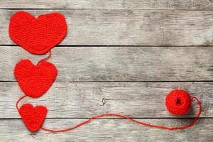 tres corazones de punto rojo sobre un fondo de madera gris, que simbolizan el amor y la familia. relación familiar, vínculos. foto