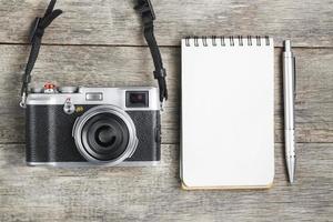 Classic camera with blank notepad page and gray pen on gray wooden, vintage desk photo