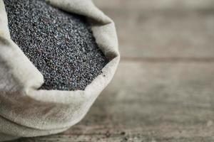Poppy seeds in a burlap bag on a vintage wooden gray background. The tasty and useful seeds rich with protein and oils. photo