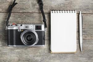 Classic camera with blank notepad page and gray pen on gray wooden, vintage desk photo