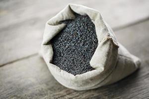 Poppy seeds in a burlap bag on a vintage wooden gray background. The tasty and useful seeds rich with protein and oils. photo