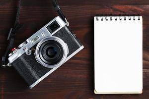 Blank notepad page and modern camera in classic style on dark brown wooden table photo