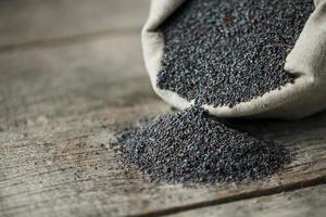 Poppy seeds in a burlap bag on a vintage wooden gray background. The tasty and useful seeds rich with protein and oils. photo