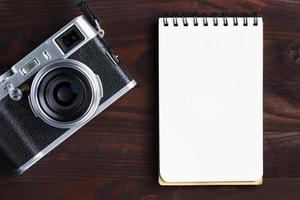 Blank notepad page and modern camera in classic style on dark brown wooden table photo