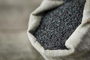 Poppy seeds in a burlap bag on a vintage wooden gray background. The tasty and useful seeds rich with protein and oils. photo