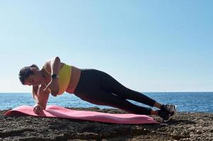 FITNESS WOMAN IN SPORTS SET TRAINING WITH ELASTIC BAND, WEIGHTS, GYM EXERCISES, IN FRONT OF THE WATER. photo