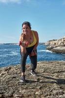 Latin woman, middle-aged, wearing sportswear, training, doing physical exercises, plank, sit-ups, climber's step, burning calories, keeping fit, outdoors by the sea, wearing headphones, smart watch photo