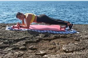 Latin woman, middle-aged, wearing sportswear, training, doing physical exercises, plank, sit-ups, climber's step, burning calories, keeping fit, outdoors by the sea, wearing headphones, smart watch photo