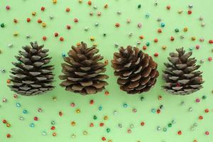 Pine fir cones of coniferous tree and jingle bells isolated on green background. Creative christmas holiday composition. Decoration for postcard. Top view, copy space, flat lay, close up photo