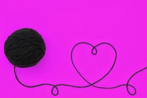 Panoramic top view of knitting black wool ball and thread in shape of heart on violet background. World knitting day greeting card, idea for poster, banner. Craft, handmade, crochet flatlay concept photo