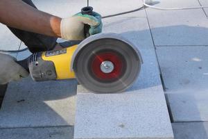 Hands of worker with electric grinder trims paving slabs on the construction site. Concept of laying new sidewalk tile. Stone cutting equipment. Road works. Civil engineering. Repair asphalt. Close-up photo