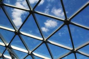 Transparent glass dome roof of modern design style pavilion building with geometric metal construction pattern. View of blue sky and clouds. Abstract structure triangle high-tech architecture window. photo