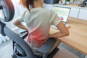 mujer con dolor de espalda durante mucho tiempo en el lugar de trabajo. por piriforme, lumbalgia, dolor de cintura, lumbago, riñón, reumatismo y compresión espinal. síndrome de oficina y concepto ergonómico foto