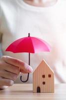 Businesswoman hand holding red Umbrella cover wooden Home model. real estate, insurance and property concepts photo