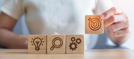 Woman hand holding dartboard above Gear, magnifying and Lightbulb icon block. business planning process, goal, strategy, target, mission, action, research, teamwork and idea concept photo