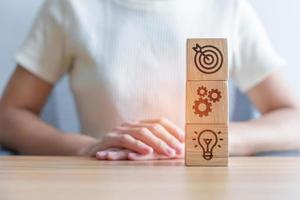 dartboard above Gear and Lightbulb icon block on desk. business planning process, goal, strategy, target, mission, action, objective, teamwork and idea concept photo