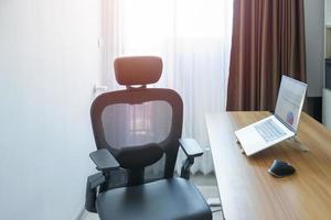 silla ergonómica y mesa ajustable con computadora portátil en un lugar de trabajo moderno. buena postura para evitar el síndrome de oficina, dolor de espalda, dolor de hombro, fibromialgia y dolor de cuello foto