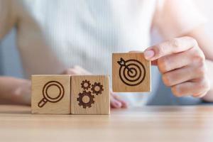 Woman hand holding dartboard, Gear and Lightbulb icon block on table. business planning process, goal, strategy, target, mission, action, objective, teamwork and research concept photo