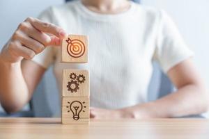 Woman hand holding dartboard above Gear and Lightbulb icon block. business planning process, goal, strategy, target, mission, action, objective, teamwork and idea concept photo
