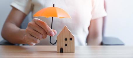 Businesswoman hand holding orange Umbrella cover wooden Home model. real estate, insurance and property concepts photo