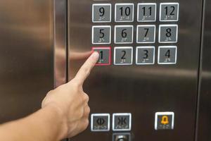 el dedo de la mano presiona el botón del ascensor, la mujer que usa el ascensor en la oficina o el apartamento foto
