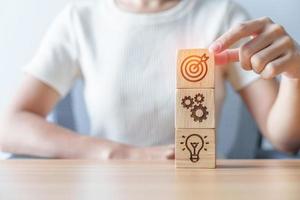 Woman hand holding dartboard above Gear and Lightbulb icon block. business planning process, goal, strategy, target, mission, action, objective, teamwork and idea concept photo