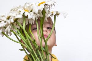 A cute boy with a beautiful bouquet of large daisies. Portrait of a child, funny and cute facial expression. Selective focus. photo