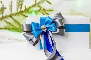 A Christmas gift decorated with a beautiful bow on a light background with a twig, if. Selective focus. the concept of Christmas and New Year. photo