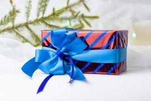 A Christmas gift decorated with a beautiful bow on a light background with a twig, if. Selective focus. the concept of Christmas and New Year. photo