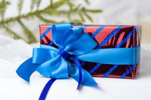 A Christmas gift decorated with a beautiful bow on a light background with a twig, if. Selective focus. the concept of Christmas and New Year. photo