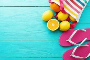 Summer fun time and fruits on blue wooden background. Mock up and picturesque. Orange, lemon fruit in bag and flip flops on the floor. Top view and copy space photo