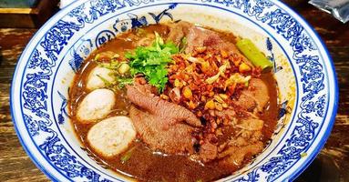 Close up Thai noodle with Australian Wagyu beef, stewed pork, meatball, liver and blood soup on bowl. The famous food in Thailand and Asia. photo