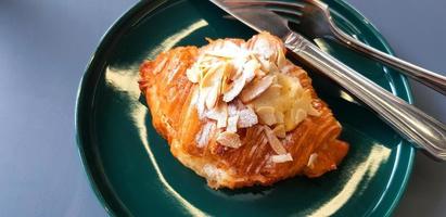 Croissant with icing sugar and almond sliced with stainless steel knife in green dish on gray table with copy space. Crispy bread in plate on grey background. Food for eat with coffee or tea at caf. photo